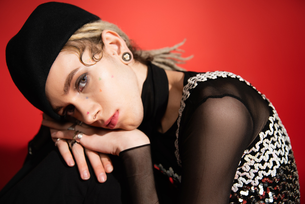 portrait of queer person in black beret and elegant top with sequins looking at camera on red background - Fotografie, Obrázek