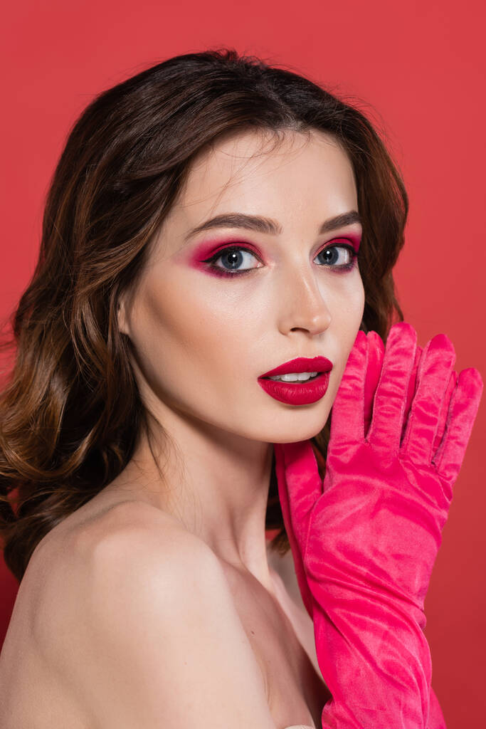 portrait of young woman with trendy magenta color eye shadow looking at camera isolated on pink  - Foto, Imagem