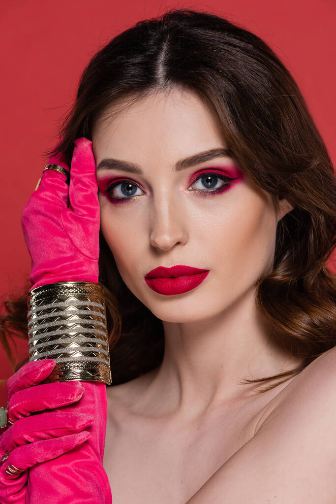 portrait of young woman in magenta color gloves with golden rings and bracelet posing isolated on pink  - Foto, afbeelding