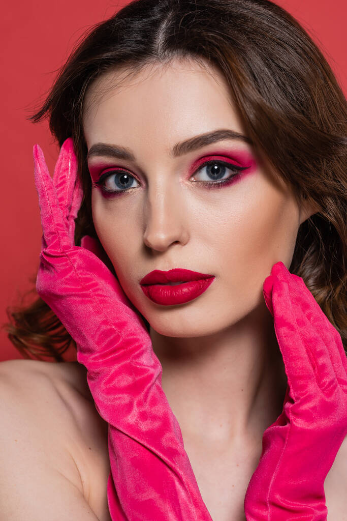 portrait of young woman with magenta color makeup and bright gloves looking at camera isolated on pink  - Фото, изображение