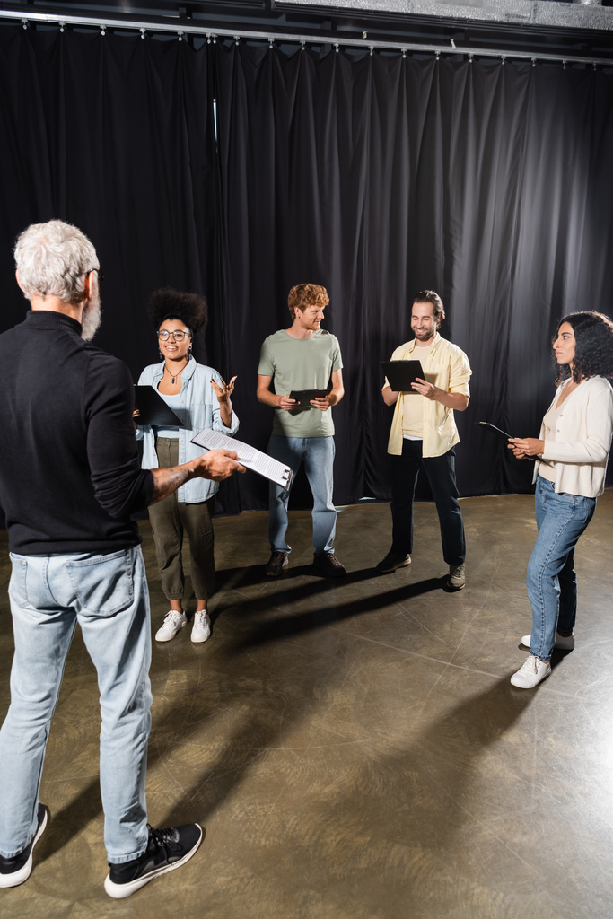 multiethnic actors standing with screenplays near grey haired art director in theater  - Photo, image