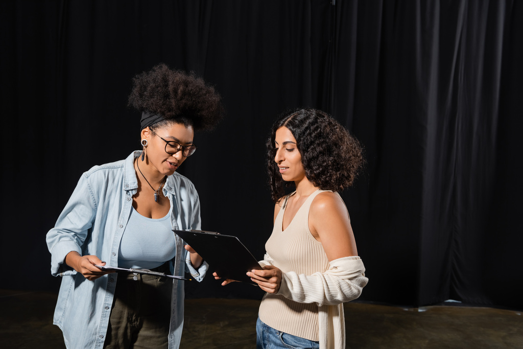 young interracial actresses looking at clipboards with scenarios in theater - Fotografie, Obrázek