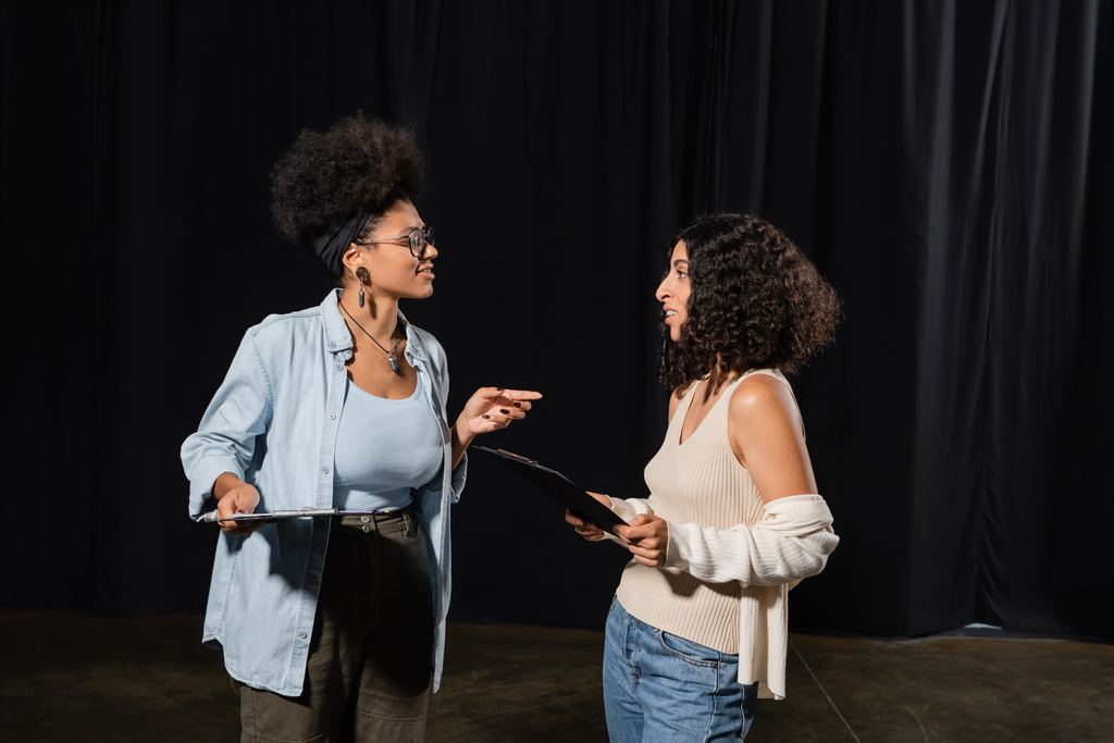 african american woman with clipboard pointing with finger while talking to multiracial actress in theater - 写真・画像