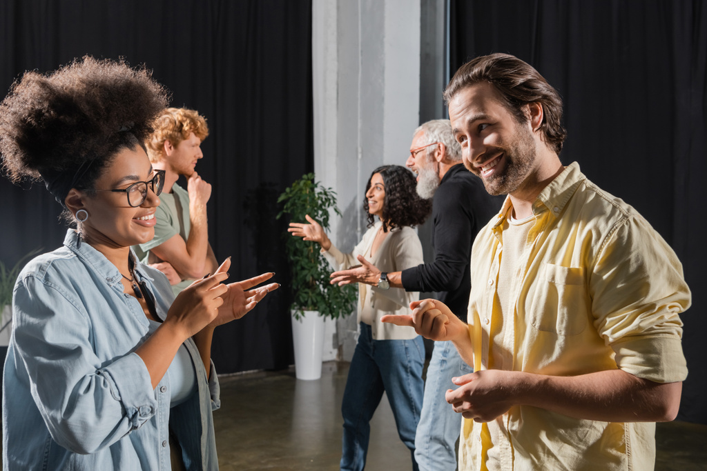 side view of smiling multiethnic students and teacher of acting skills talking and gesturing in theater school - Photo, Image
