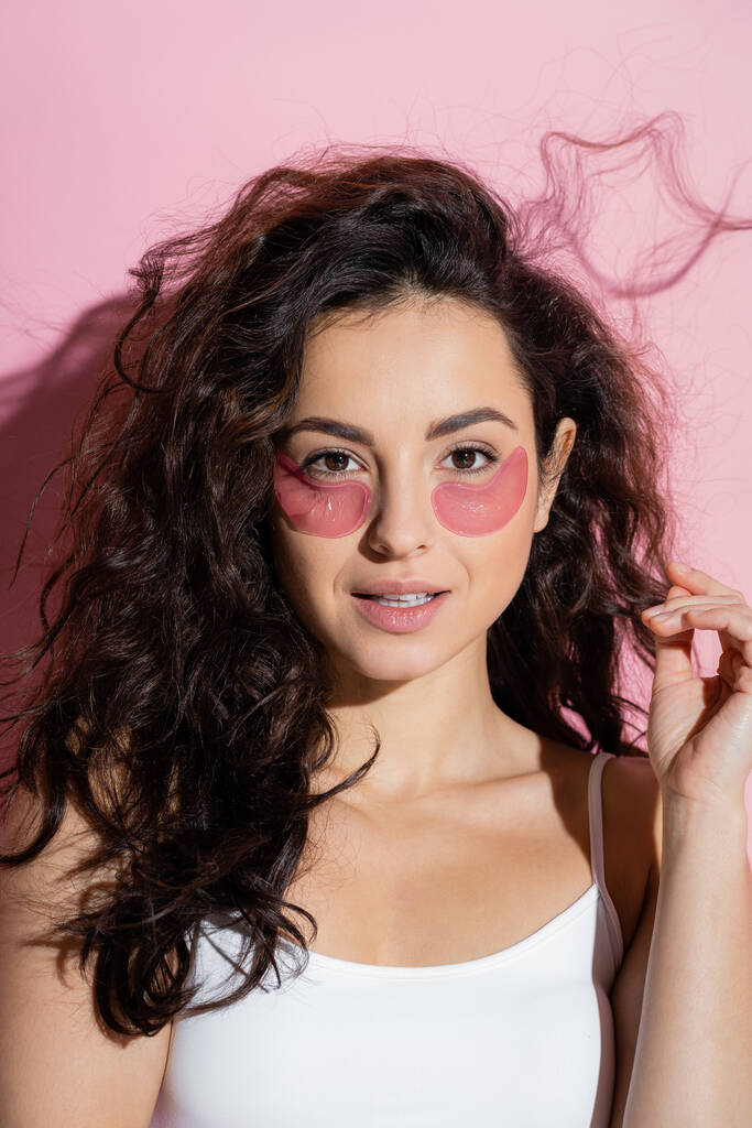 Curly young woman with hydrogel eye patches on pink background  - Fotó, kép