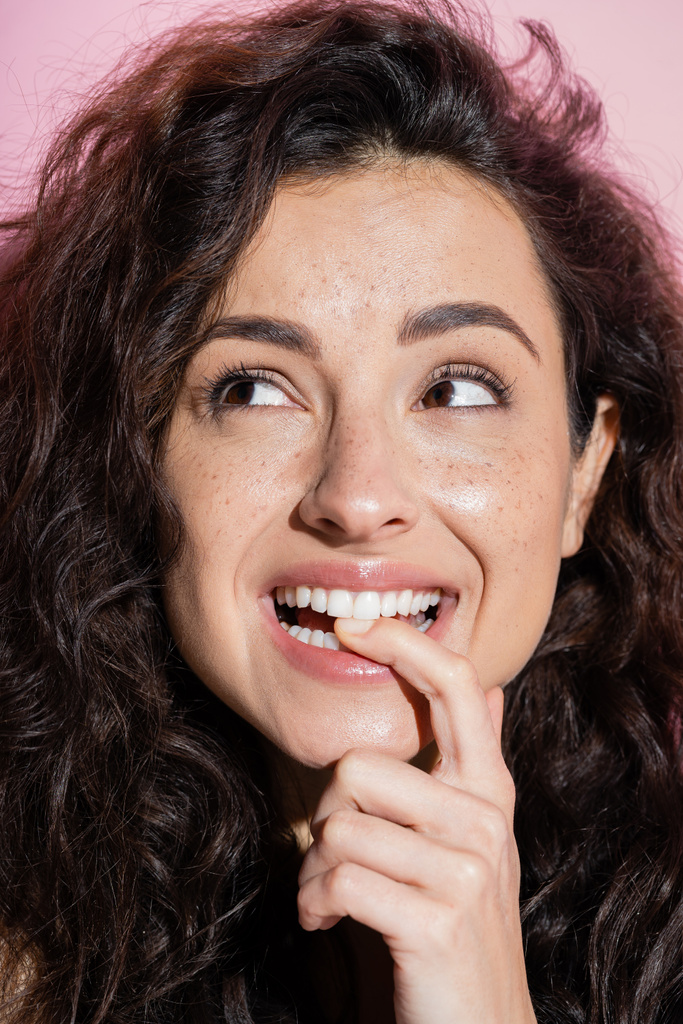 Pretty brunette woman with freckles holding finger near teeth isolated on pink  - Photo, image