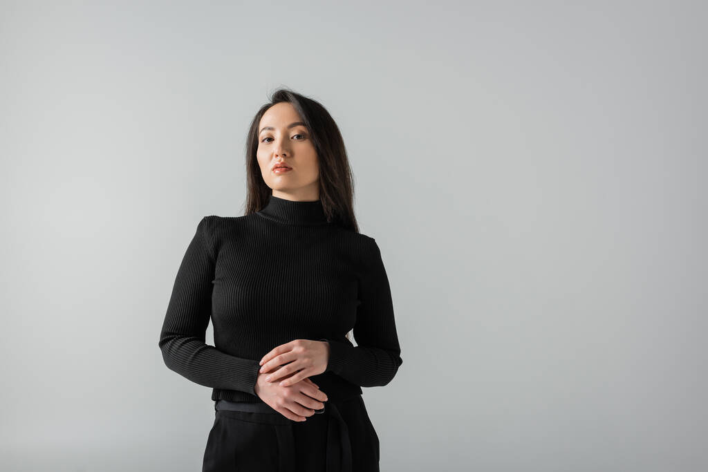 brunette asian businesswoman in black turtleneck looking at camera isolated on grey  - Фото, изображение