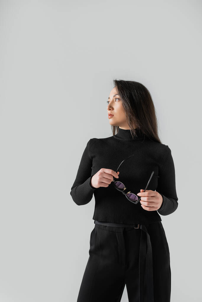 young asian businesswoman in black turtleneck holding glasses isolated on grey  - Foto, Imagem