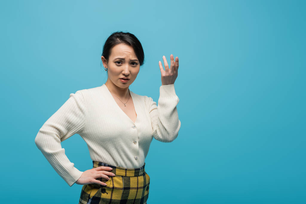 Confused asian woman in cardigan looking at camera isolated on blue  - Foto, Imagen