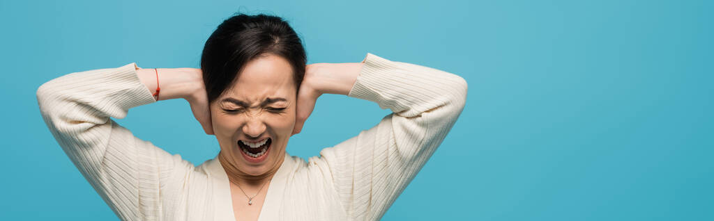 Aggressiivinen aasialainen nainen huutaa ja peittää korvat eristetty sininen, banneri  - Valokuva, kuva