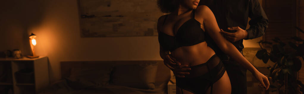 cropped view of passionate african american woman in underwear near young boyfriend in bedroom at night, banner - Foto, immagini