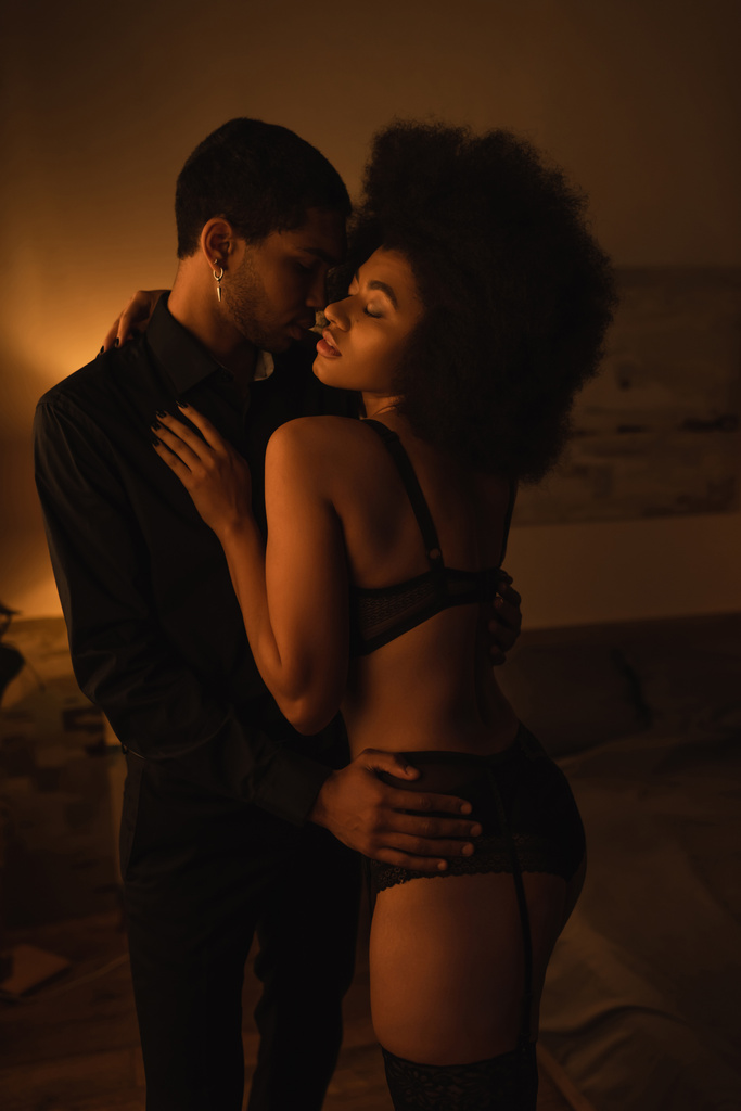seductive african american woman in sexy lingerie embracing with young boyfriend at home at night - Photo, image