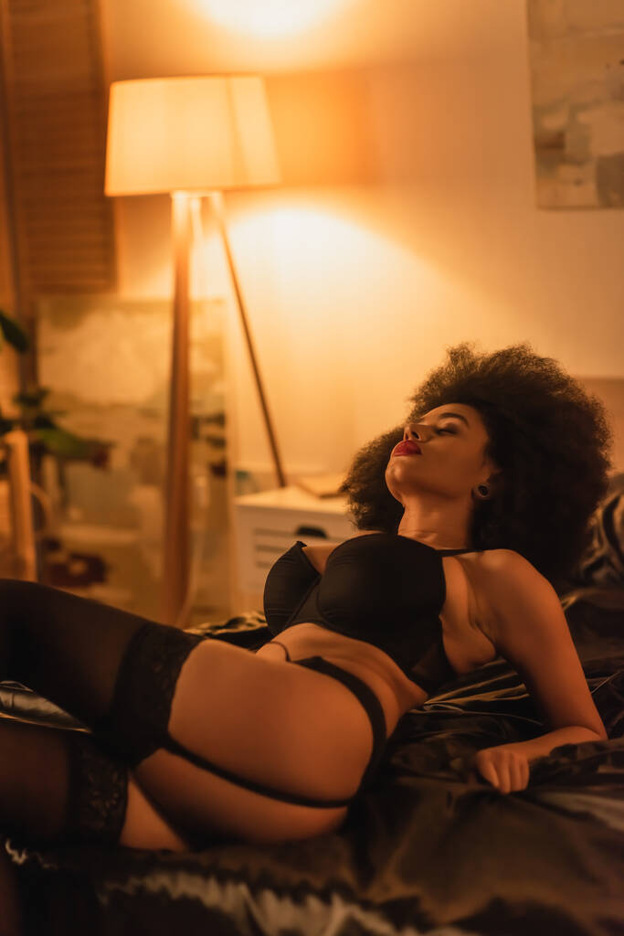 afro-américaine avec des cheveux bouclés et corps sexy couché en sous-vêtements sur le lit à la maison - Photo, image