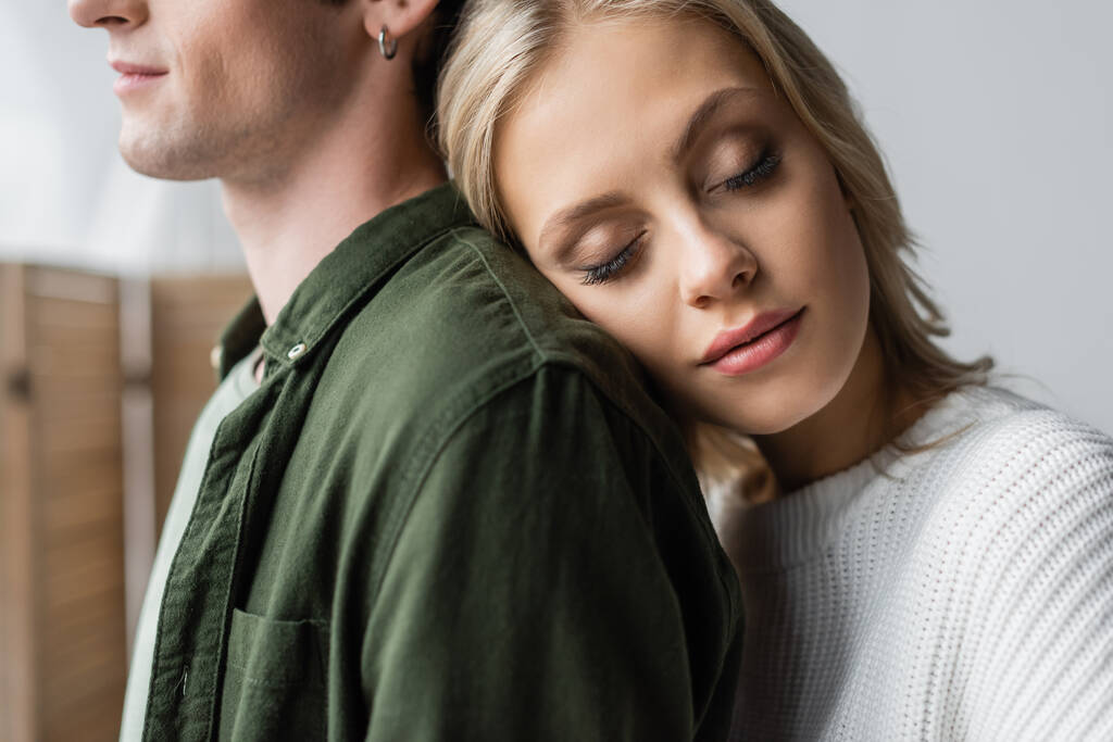 portrait of young blonde woman with closed eyes leaning on back of man - Foto, Imagem