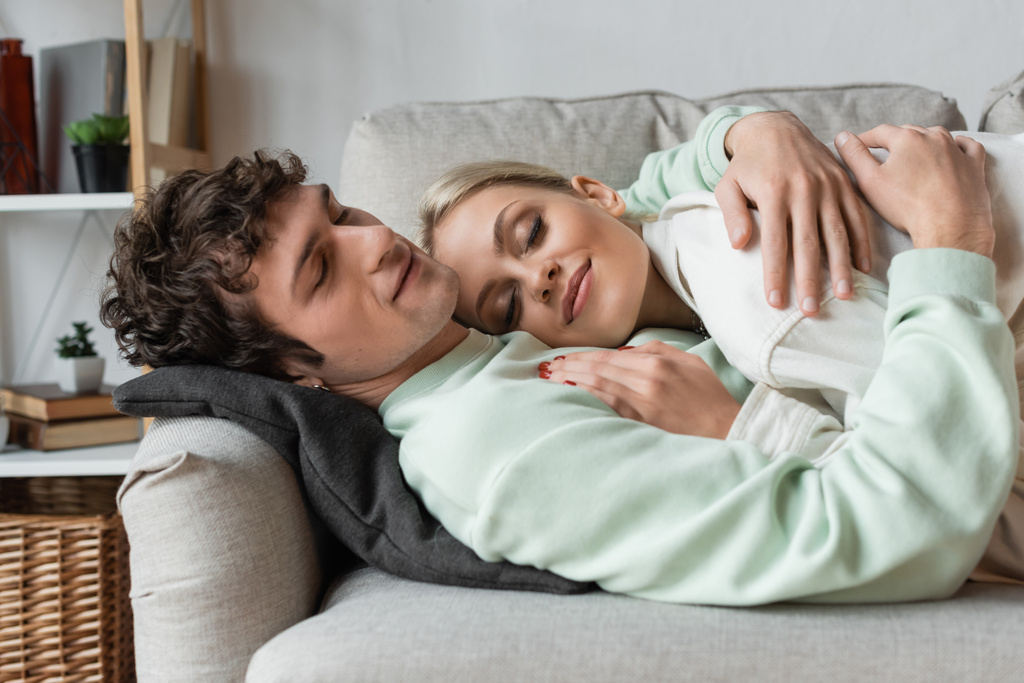 happy young man embracing girlfriend while lying on couch in living room  - Foto, imagen