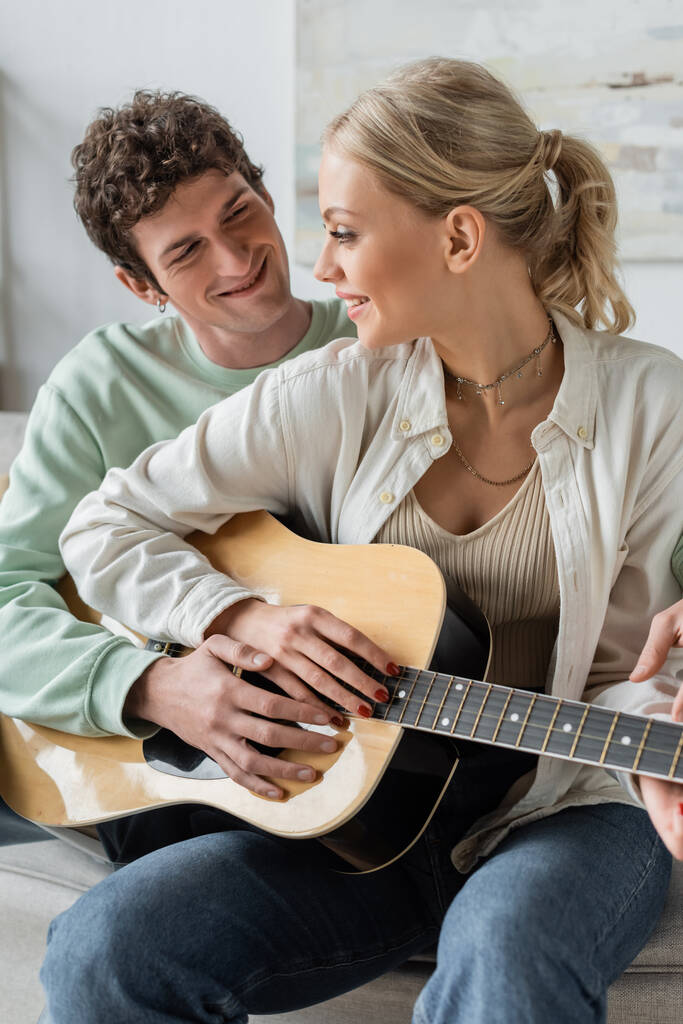 happy young couple playing acoustic guitar while sitting on couch  - Fotó, kép