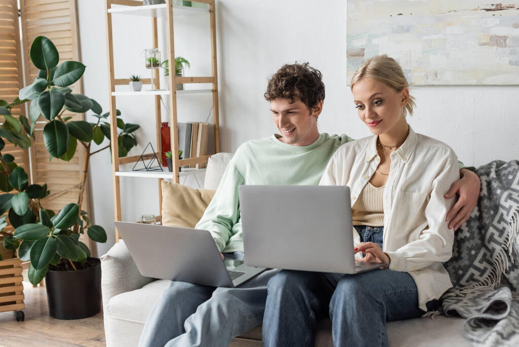 cheerful man and woman using laptops while working from home in living room  - Foto, imagen