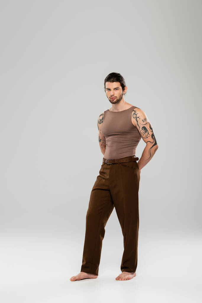 Full length of stylish tattooed man posing on grey background - Foto, afbeelding