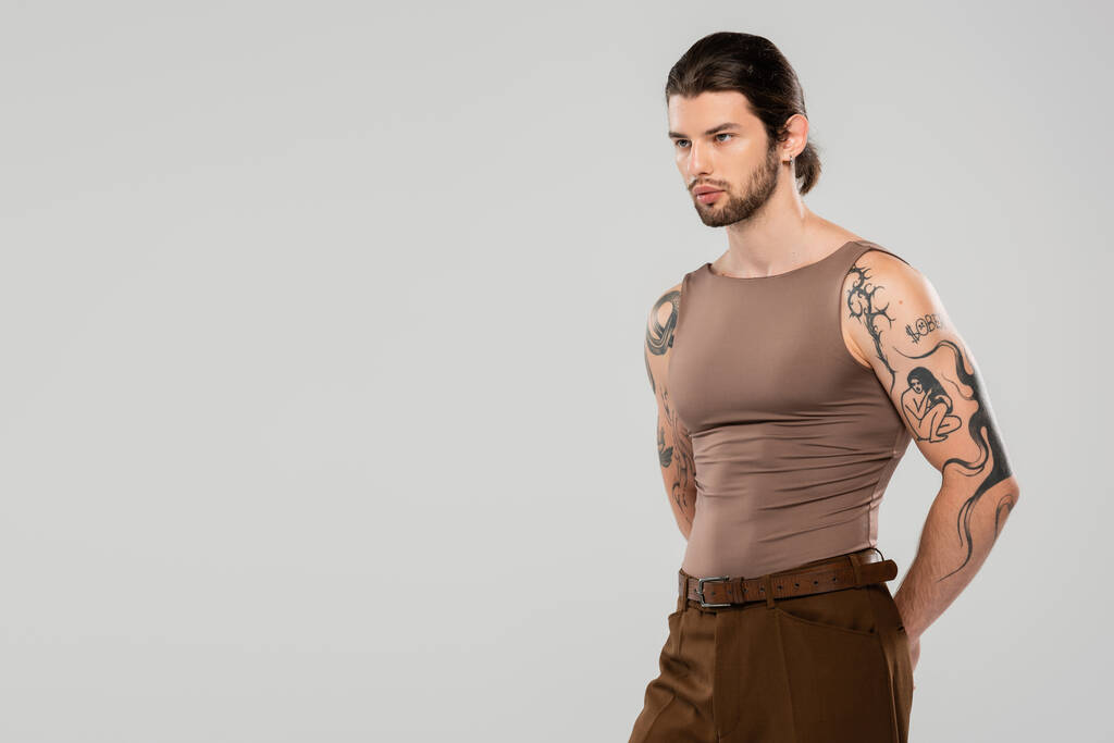 Long haired tattooed man looking away while standing isolated on grey  - Foto, Imagem