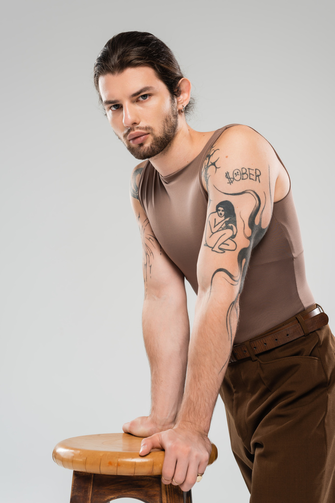 Pitkäkarvainen tatuoitu mies seisoo lähellä tuoli eristetty harmaa  - Valokuva, kuva