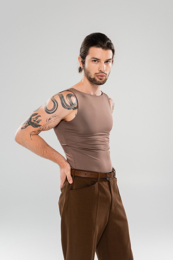 Stylish tattooed man in pants and tank top posing isolated on grey  - Фото, изображение