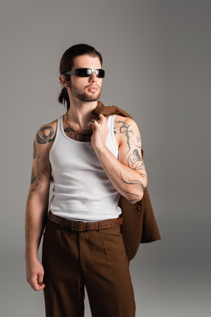 Tattooed man in sunglasses holding jacket isolated on grey  - Foto, Imagem