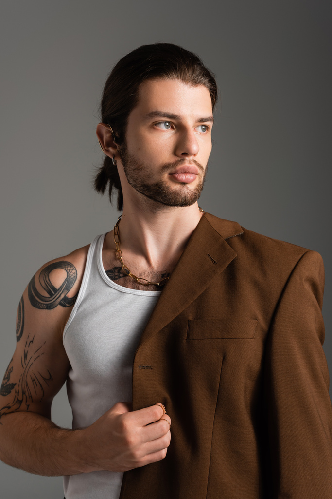 Portrait of tattooed young man in tank top holding jacket isolated on grey  - Valokuva, kuva