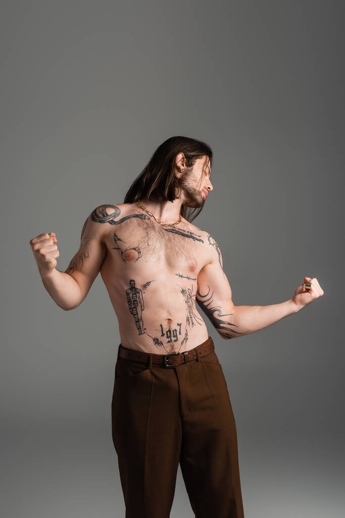 Вид збоку без сорочки татуйований чоловік тримає руки в кулаках ізольовані на сірому
  - Фото, зображення
