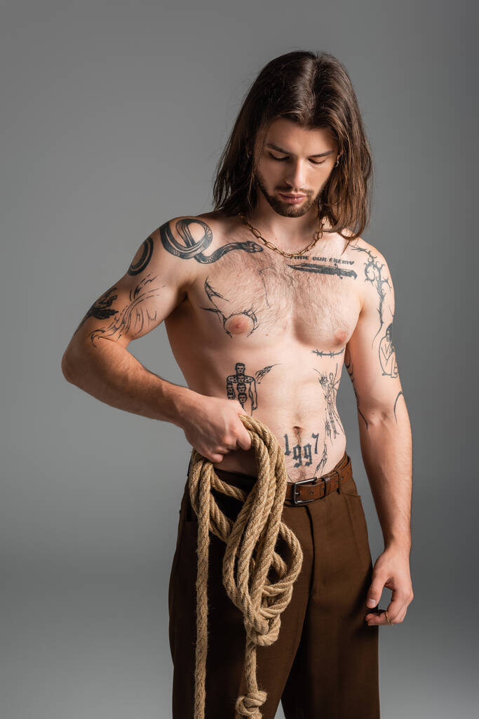 Long haired and tattooed model holding rope isolated on grey  - Foto, Imagen