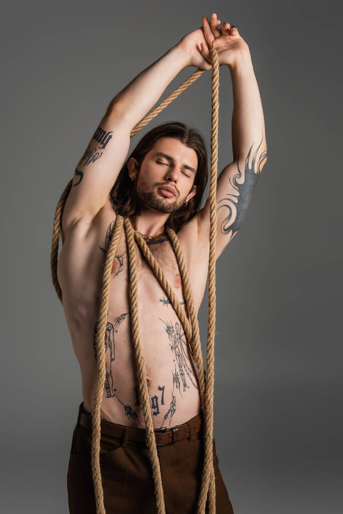Muscular tattooed model posing with rope isolated on grey  - Photo, Image