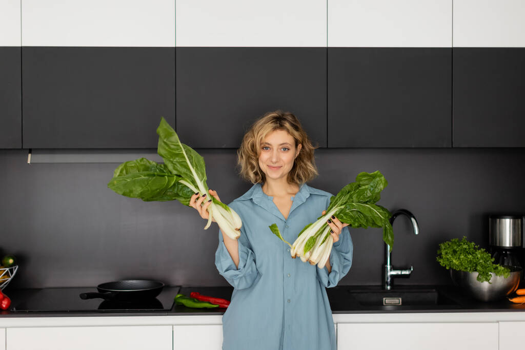 pierced young woman smiling and holding green cabbage leaves in kitchen  - Foto, Bild
