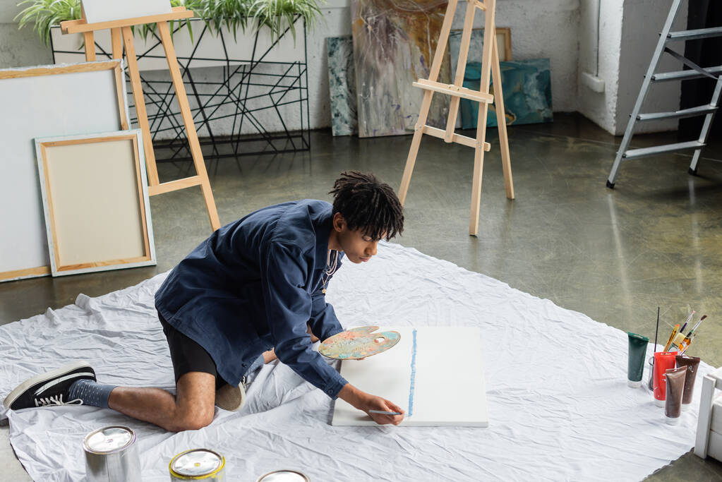 Afro-Amerikaanse kunstenaar met palet schilderen op doek in studio  - Foto, afbeelding
