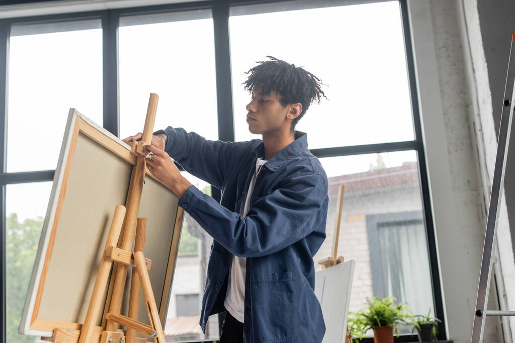 Laag gezichtsveld van jonge Afrikaans-Amerikaanse kunstenaar aanpassen canvas op houten ezel  - Foto, afbeelding