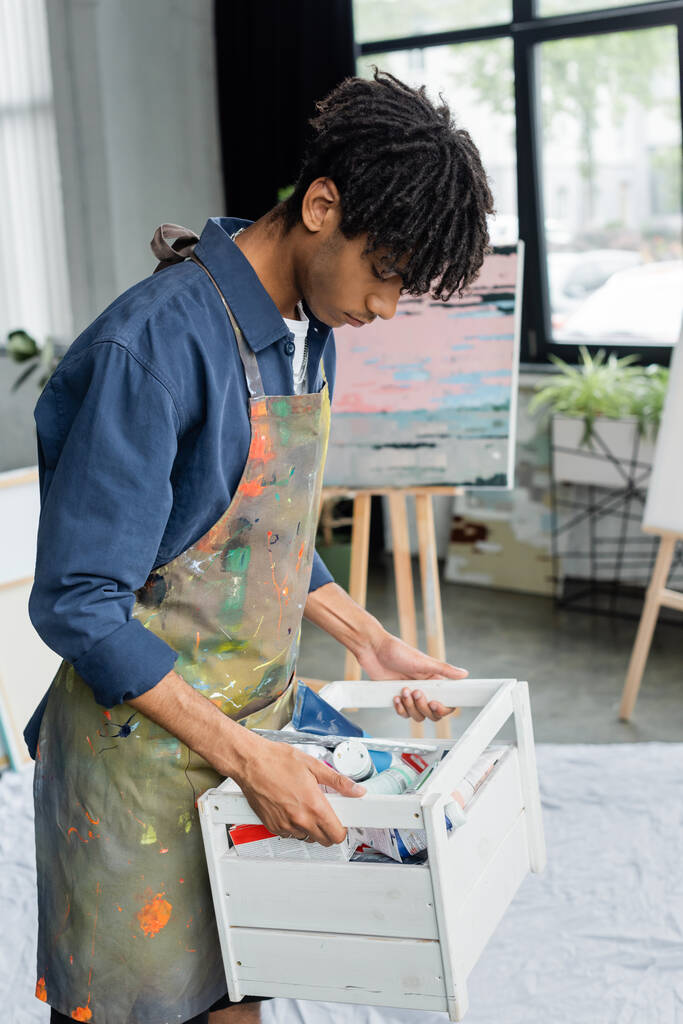 African american artist holding box with paints in studio  - 写真・画像