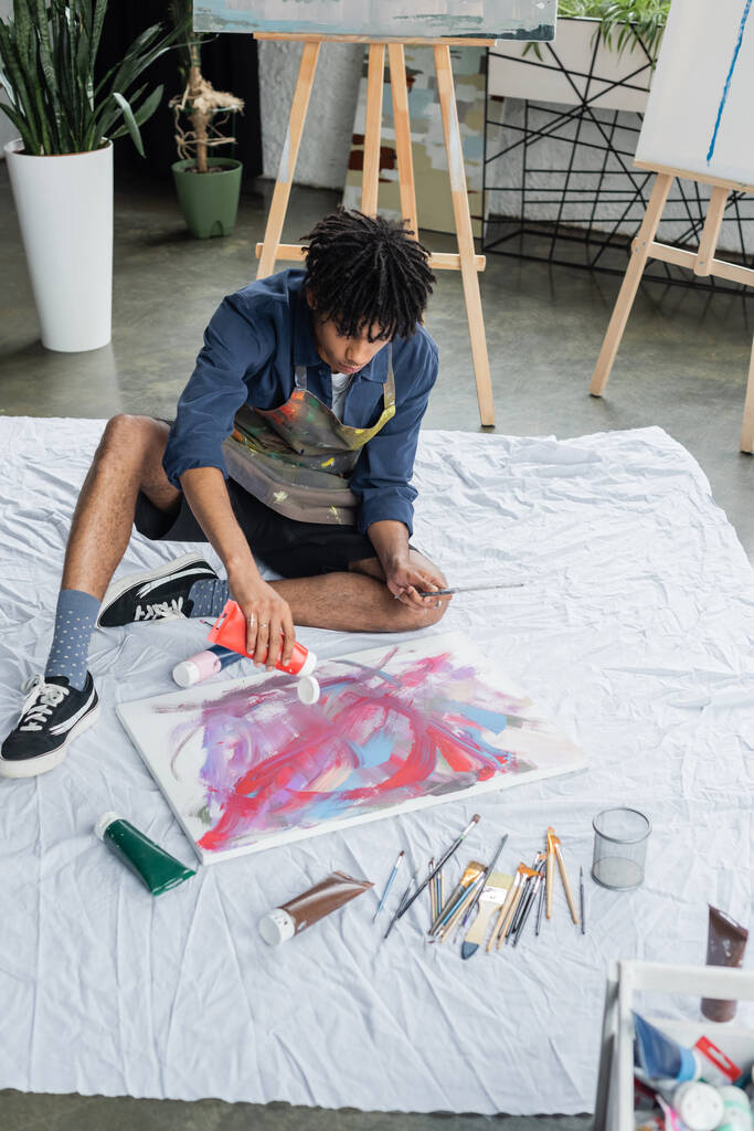 Artista afro-americano derramando tinta sobre tela em pano em estúdio  - Foto, Imagem
