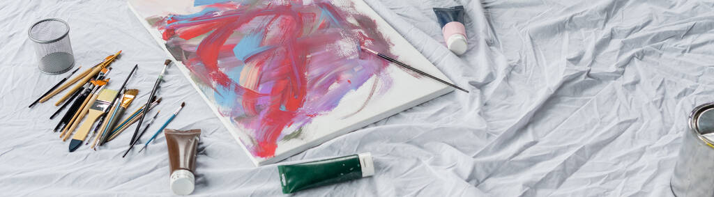 Високий кут зору пензлів біля фарб і малюнок на тканині, банер
  - Фото, зображення