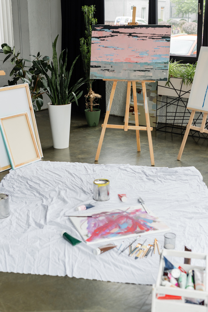 Festés festőállványon festékek és ecsetek közelében ruhán a stúdióban  - Fotó, kép
