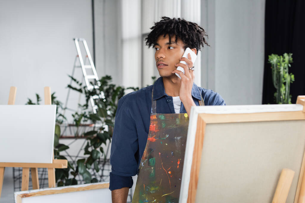 ワークショップで携帯電話で話すエプロンの若いアフリカ系アメリカ人アーティスト  - 写真・画像