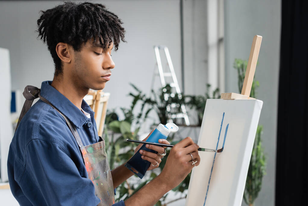 スタジオで白いキャンバスにエプロン絵を描くアフリカ系アメリカ人アーティスト  - 写真・画像