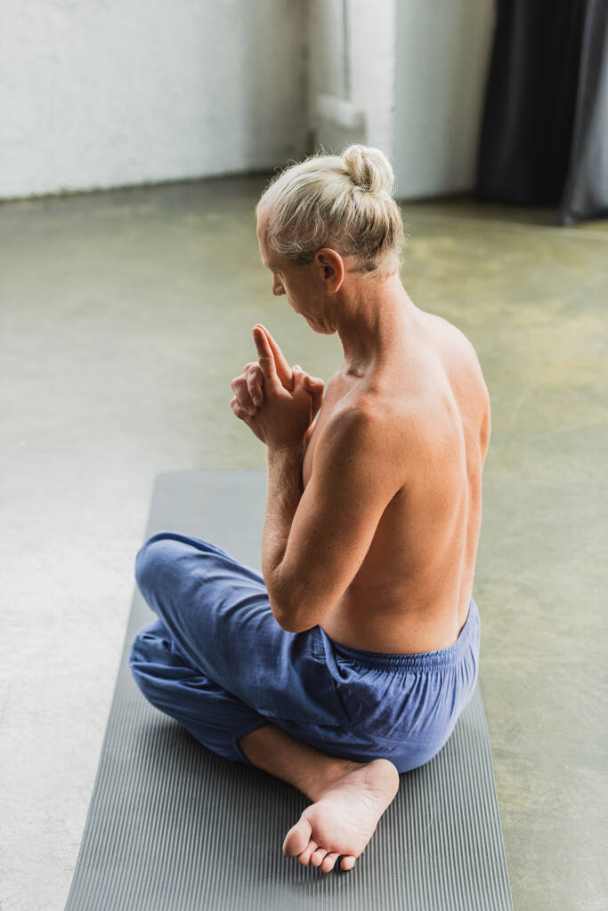 homme torse nu dans un pantalon assis dans la pose de yoga torsion et faire couronne chakra mudra - Photo, image
