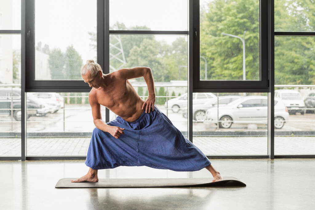 без сорочки і сірого волосатого чоловіка в штанях роблять розширений бічний кут позу в студії йоги
  - Фото, зображення