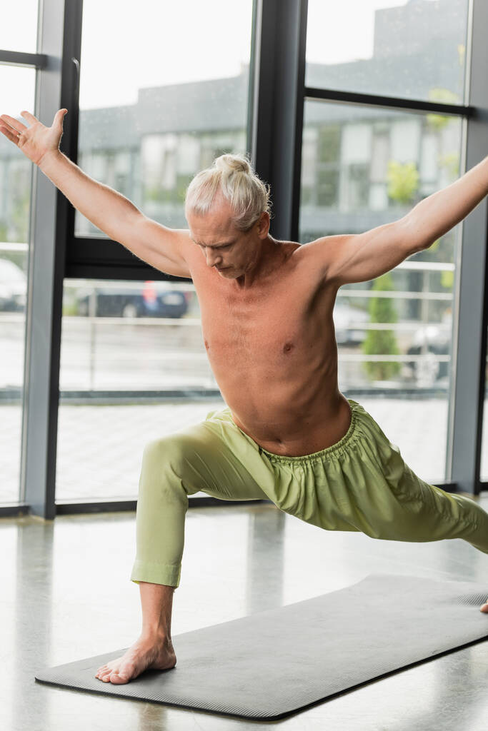 Мужчина без рубашки в зеленых штанах практикующий йогу в студии  - Фото, изображение