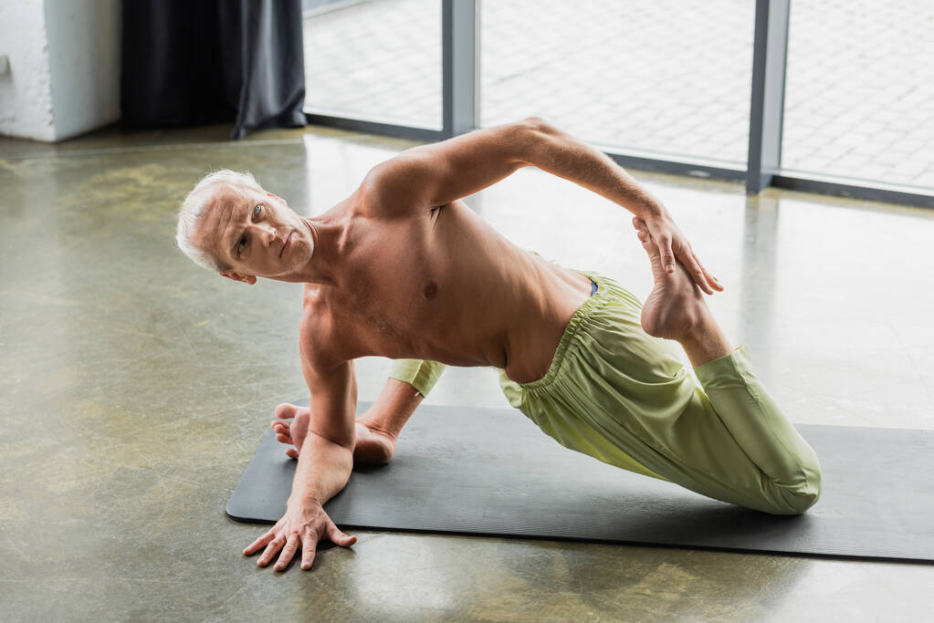 sin camisa hombre haciendo supina espina dorsal giro yoga pose en estudio  - Foto, Imagen