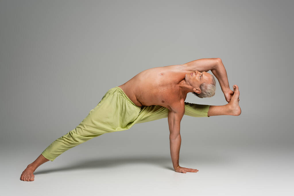 barefoot man in pants doing compass yoga pose on grey background  - Photo, Image