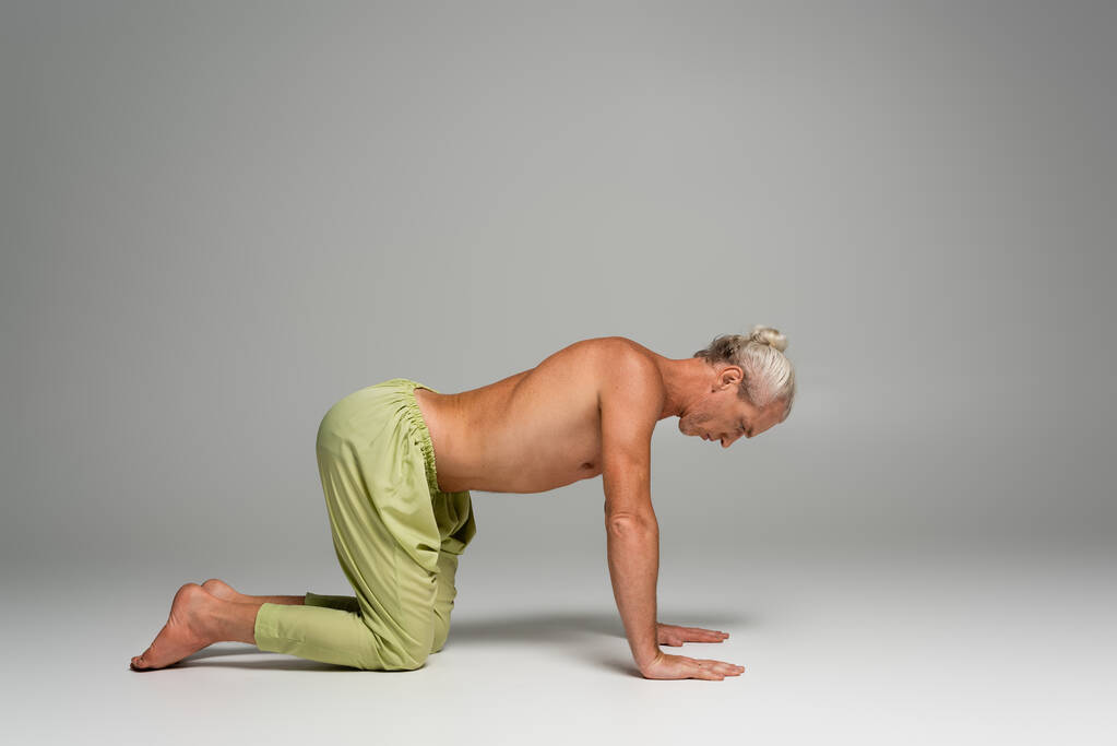 volle Länge des barfüßigen Mannes in Hose macht Kuh-Yoga-Pose auf grau  - Foto, Bild
