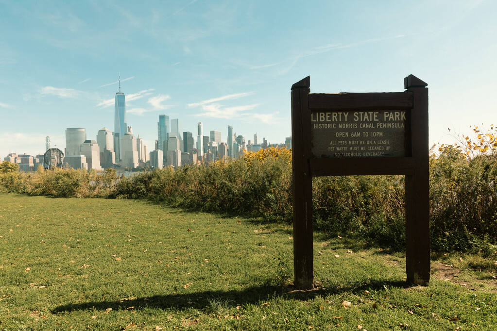 NEW YORK, USA - OCTOBER 13, 2022: board with liberty state park lettering on green lawn and cityscape with skyscrapers on background - Fotó, kép