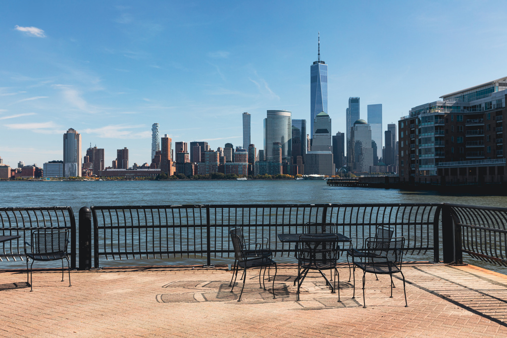 ニューヨーク市のマンハッタンの港や街並みの近くのテーブルと椅子のある堤防 - 写真・画像