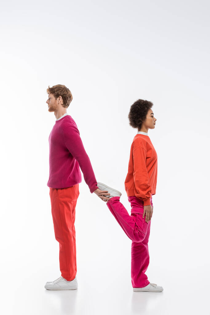 vista lateral de pareja interracial en ropa de color magenta mostrando n letra sobre fondo blanco  - Foto, Imagen