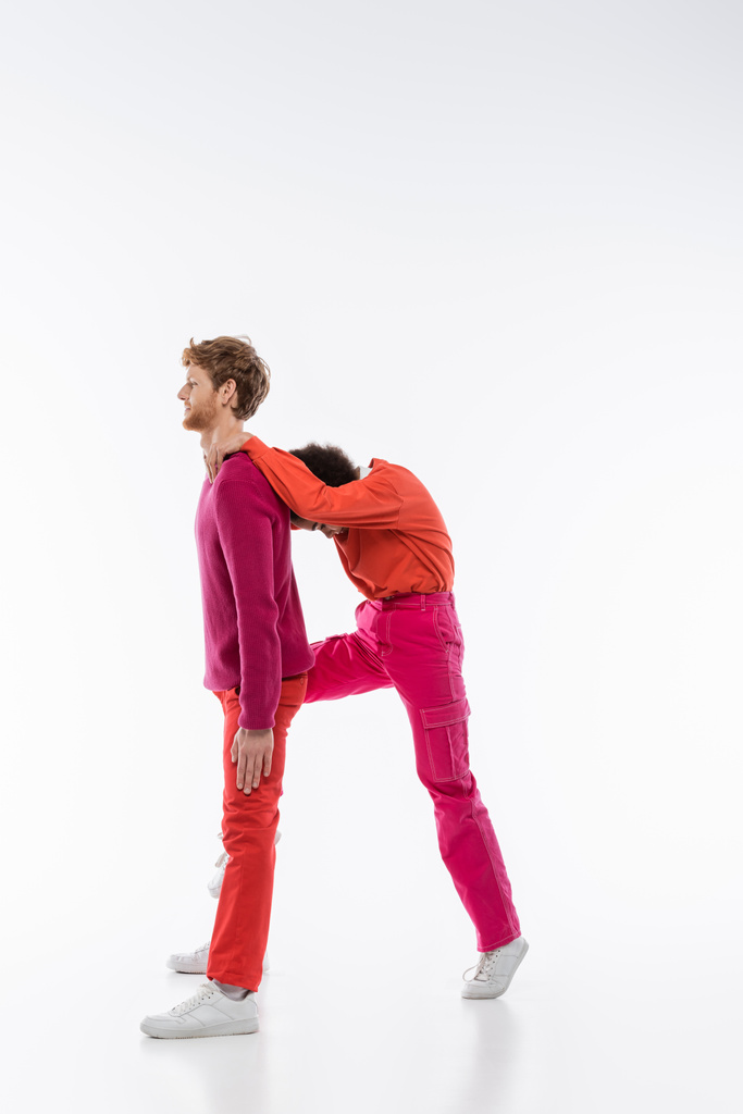 side view of multiethnic couple in magenta color clothes showing R letter on white background  - Fotografie, Obrázek