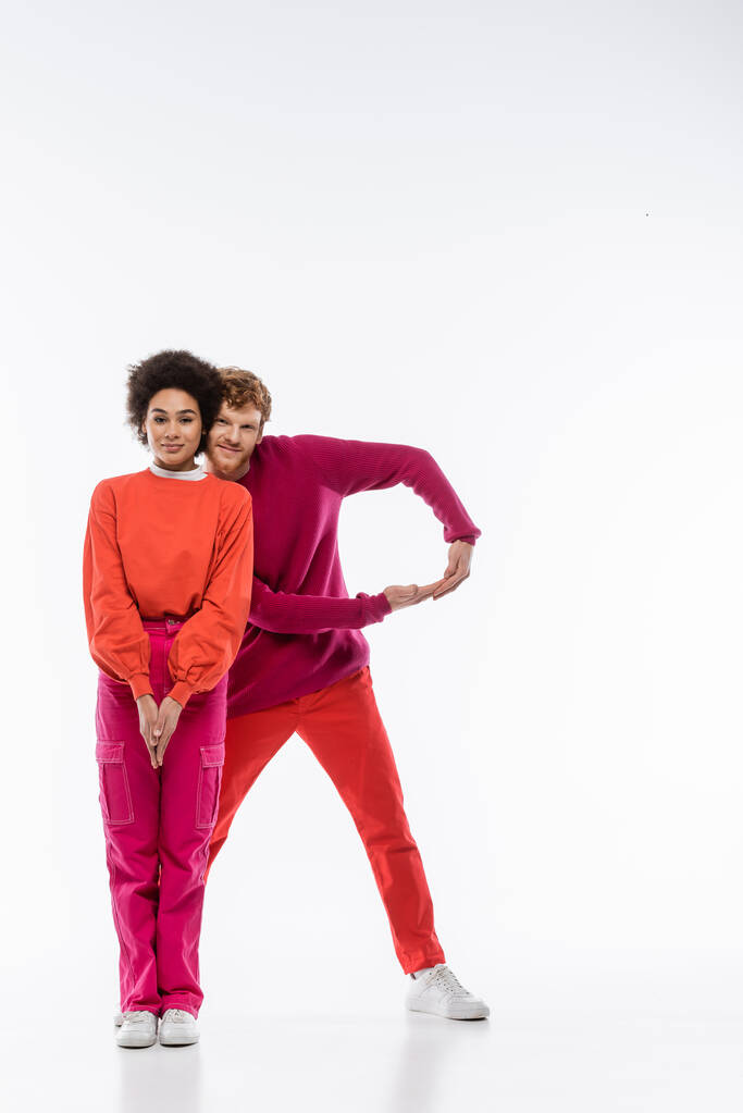 casal alegre e multiétnico em roupas de cor magenta mostrando letra R no fundo branco  - Foto, Imagem